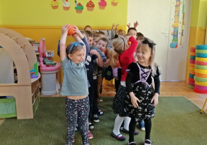 Dzieci ustawione w dwa rzędy przekazują sobie dynie nad głową.